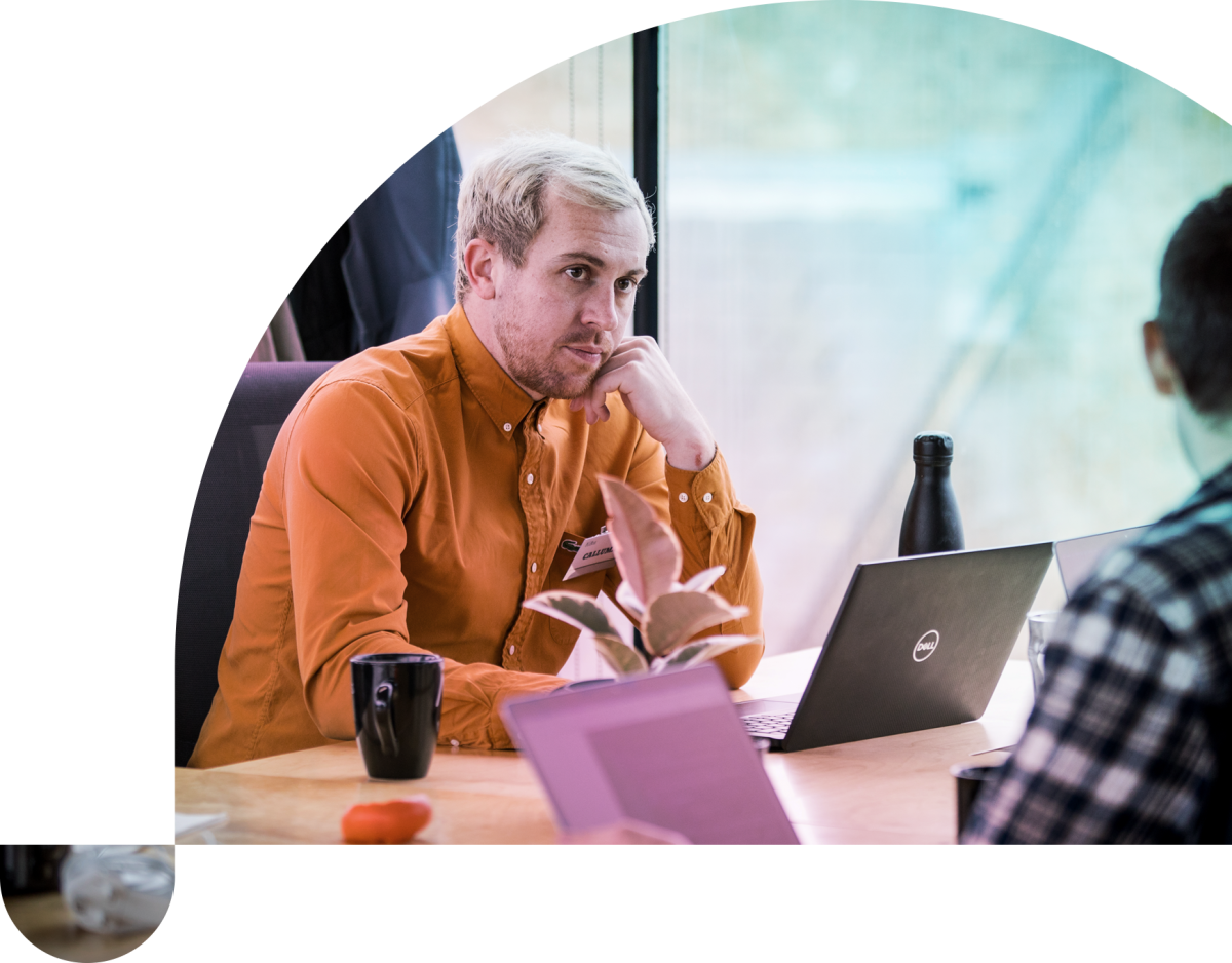 a man in an orange-brown shirt looks at his colleague, listening