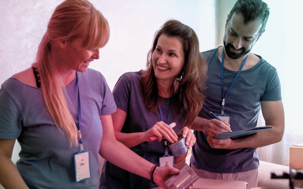 3 people wearing blue tops having a discussion while looking at tin cans