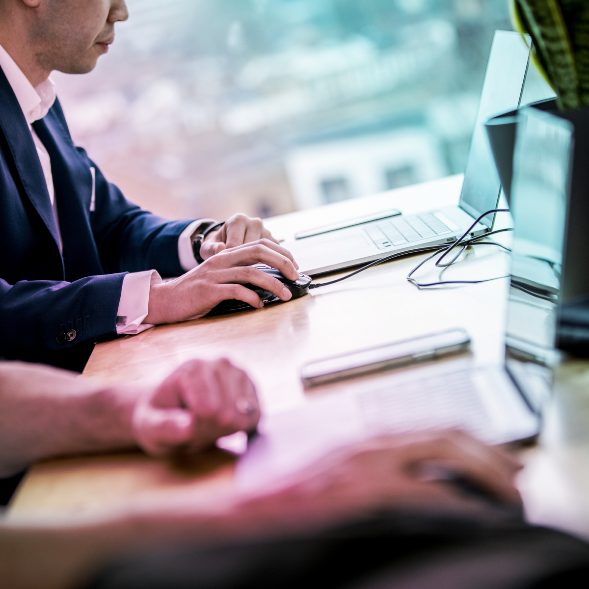 close up of a mans hands while he holds a mouse and works on a laptop