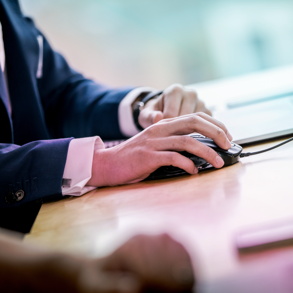 close up of a mans hands while he holds a mouse and works on a laptop