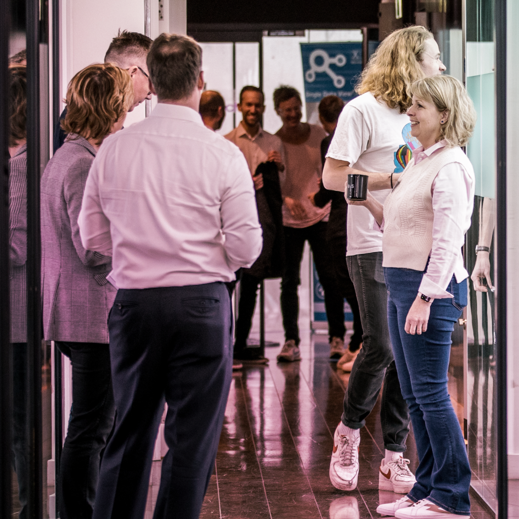 a group of people standing and talking to each other, a lady is holding a mug and standing slightly separate to the group