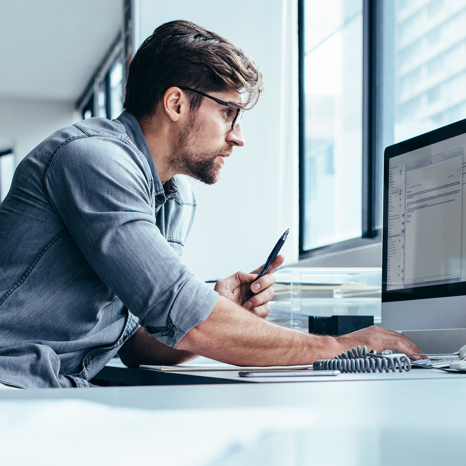 a man works intently on a computer, holding a pen