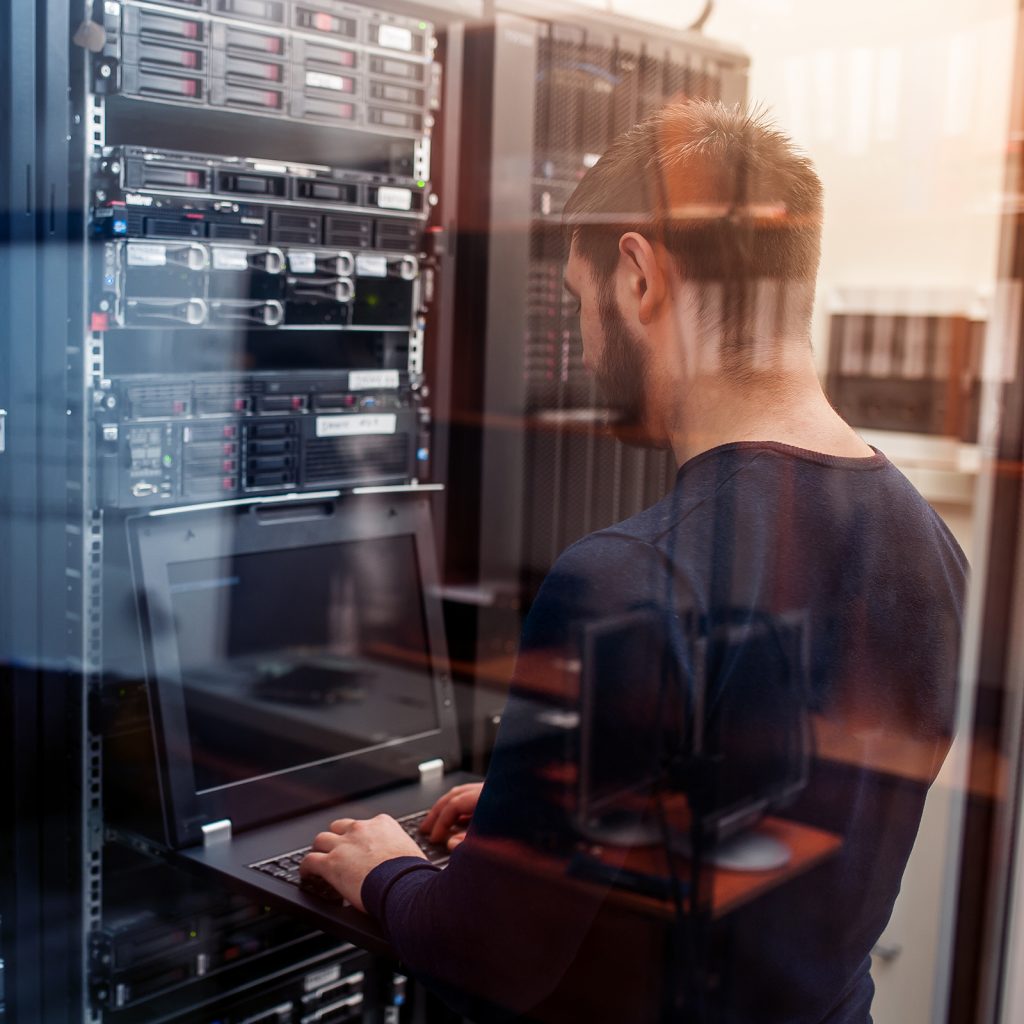 a man working on a laptop plugged into a server room