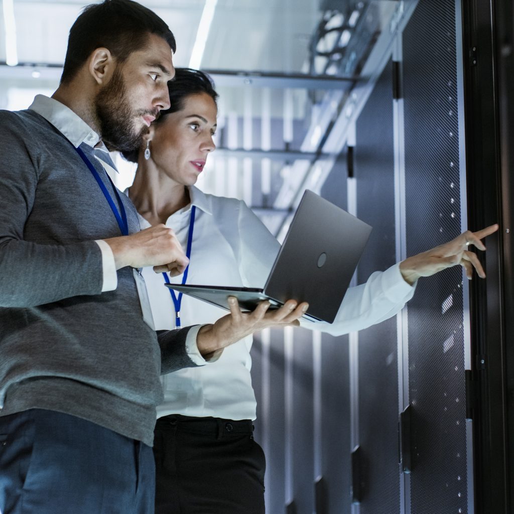 two people look at a laptop while also checking a server