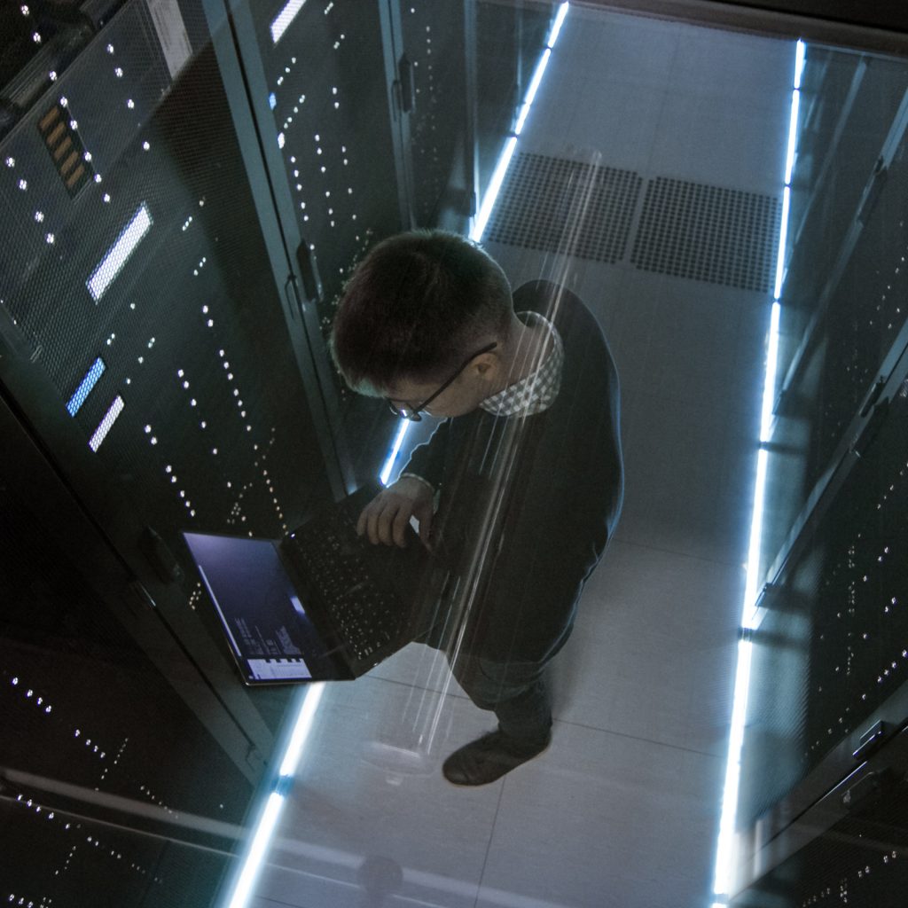 high angle shot of a man working on a laptop in a server room